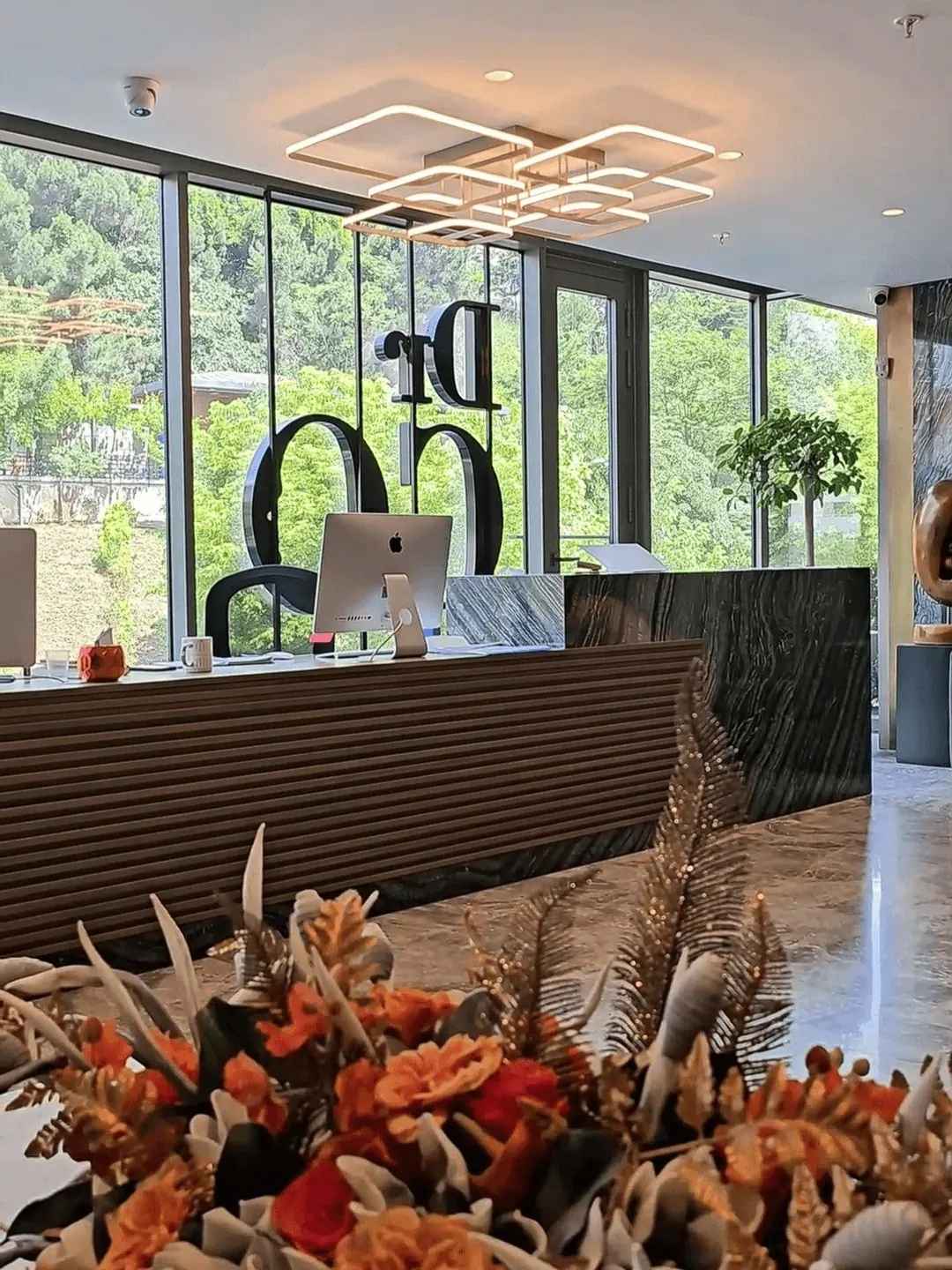 Reception desk at a modern Istanbul hair transplant clinic with large windows, greenery outside, sleek design, and floral arrangement in the foreground.