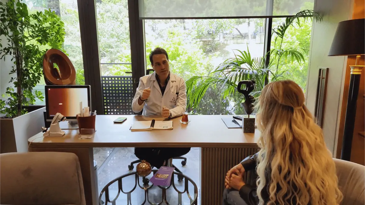 Hair transplant doctor in Istanbul consulting with a patient in a modern clinic office with large windows and greenery outside.