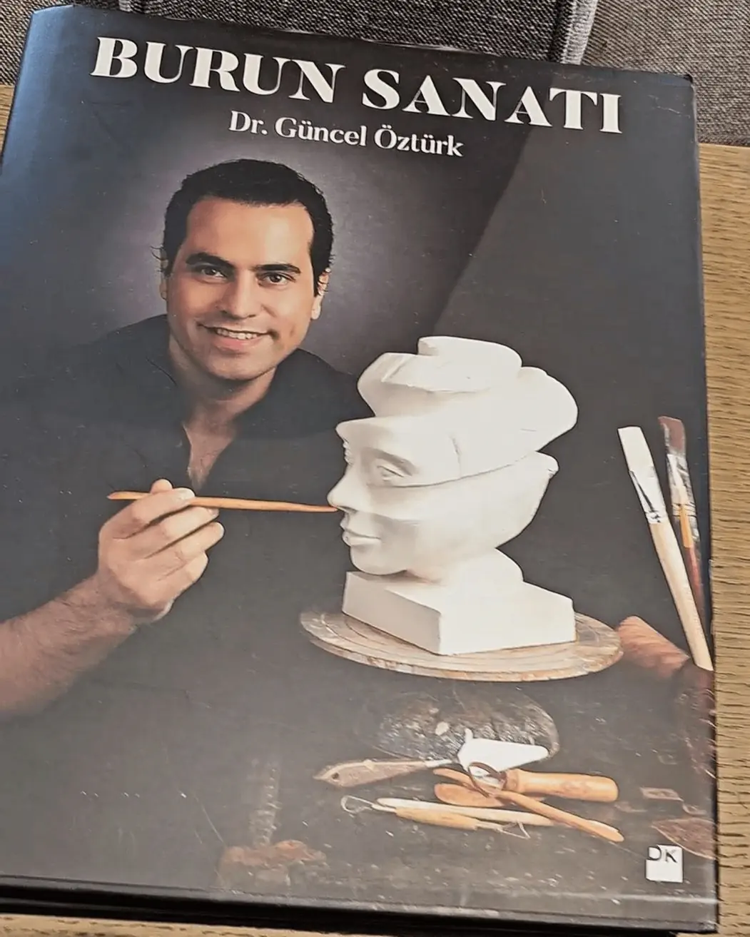 Cover of the book Burun Sanatı by Dr. Güncel Öztürk, featuring the author sculpting a bust with artistic tools on a wooden table.