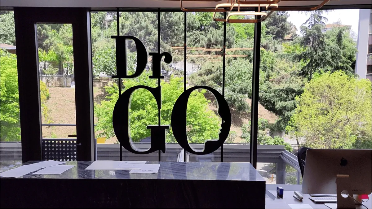 Large Dr. GO logo on glass windows at an Istanbul hair clinic, overlooking green trees and city landscape.