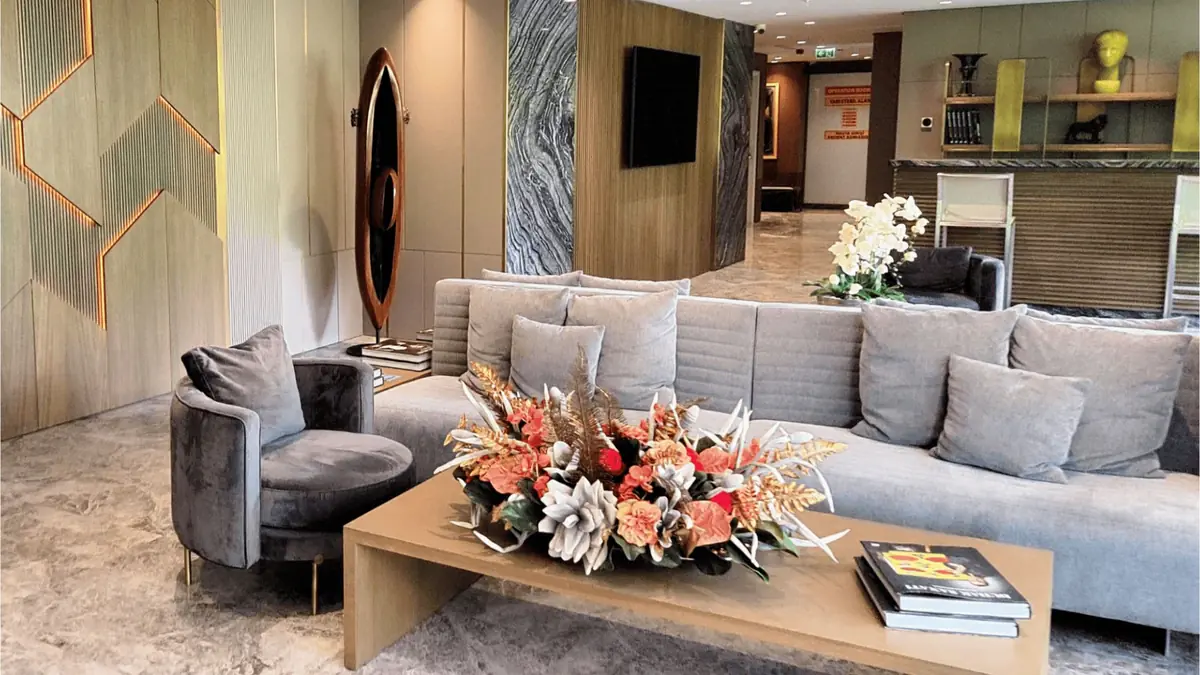 Elegant waiting room at an Istanbul hair clinic with grey sofas, modern decor, and floral centerpiece on coffee table.