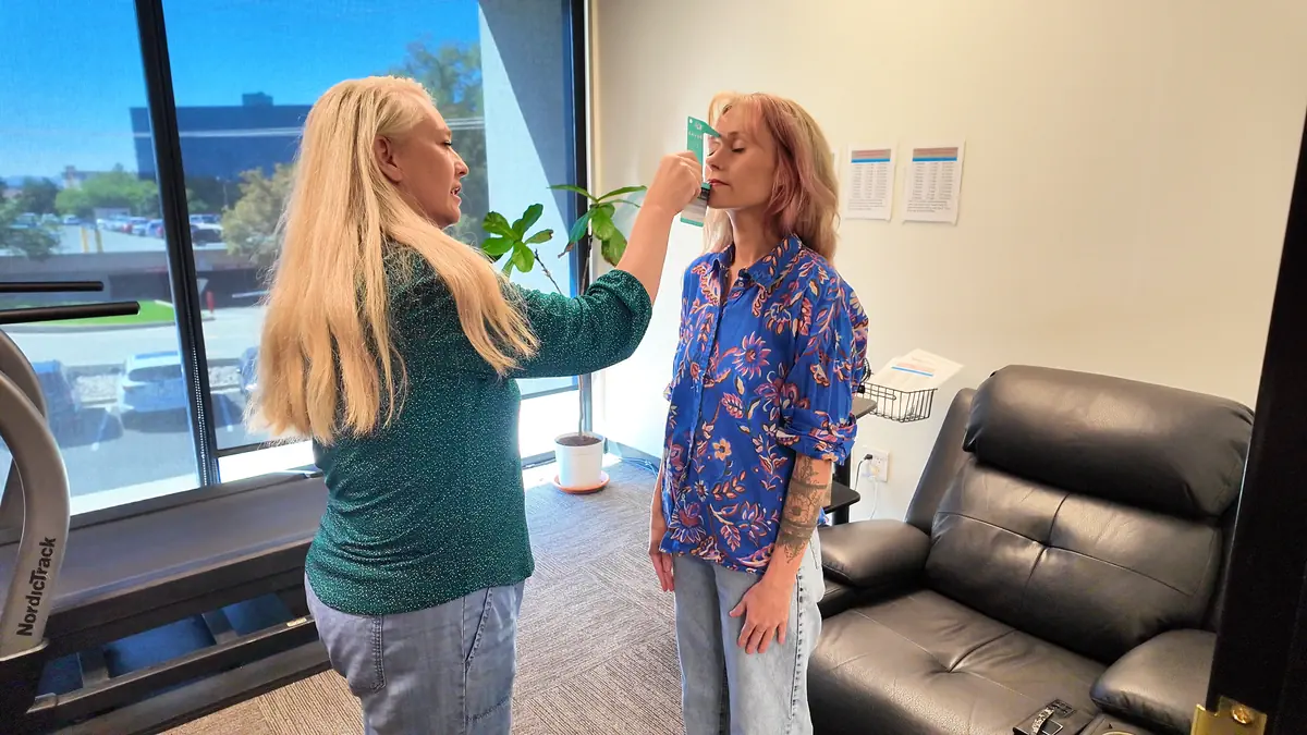 A DexaBody technician measures a woman’s breathing with a handheld metabolic testing device to prepare for a resting metabolic rate assessment.