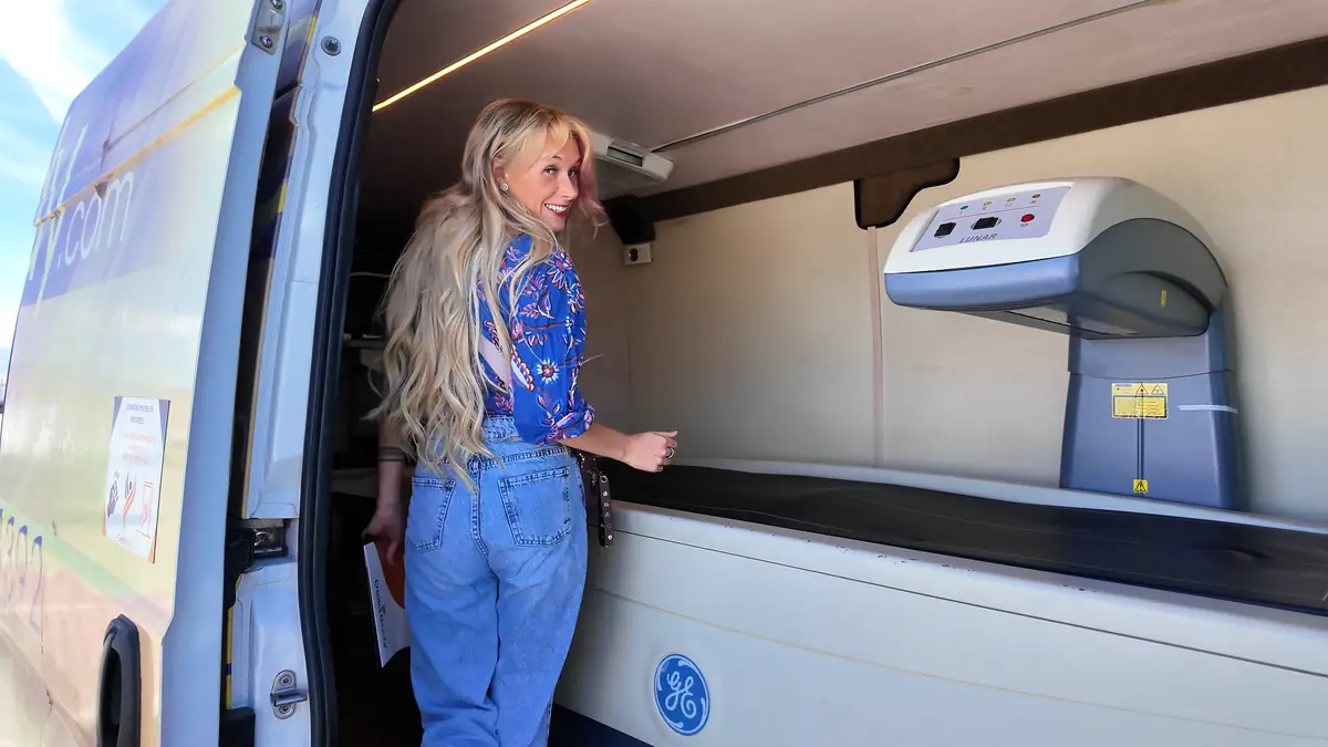 Woman stepping into a mobile Dexa scan van with a GE Lunar body composition machine for a full-body scan appointment.
