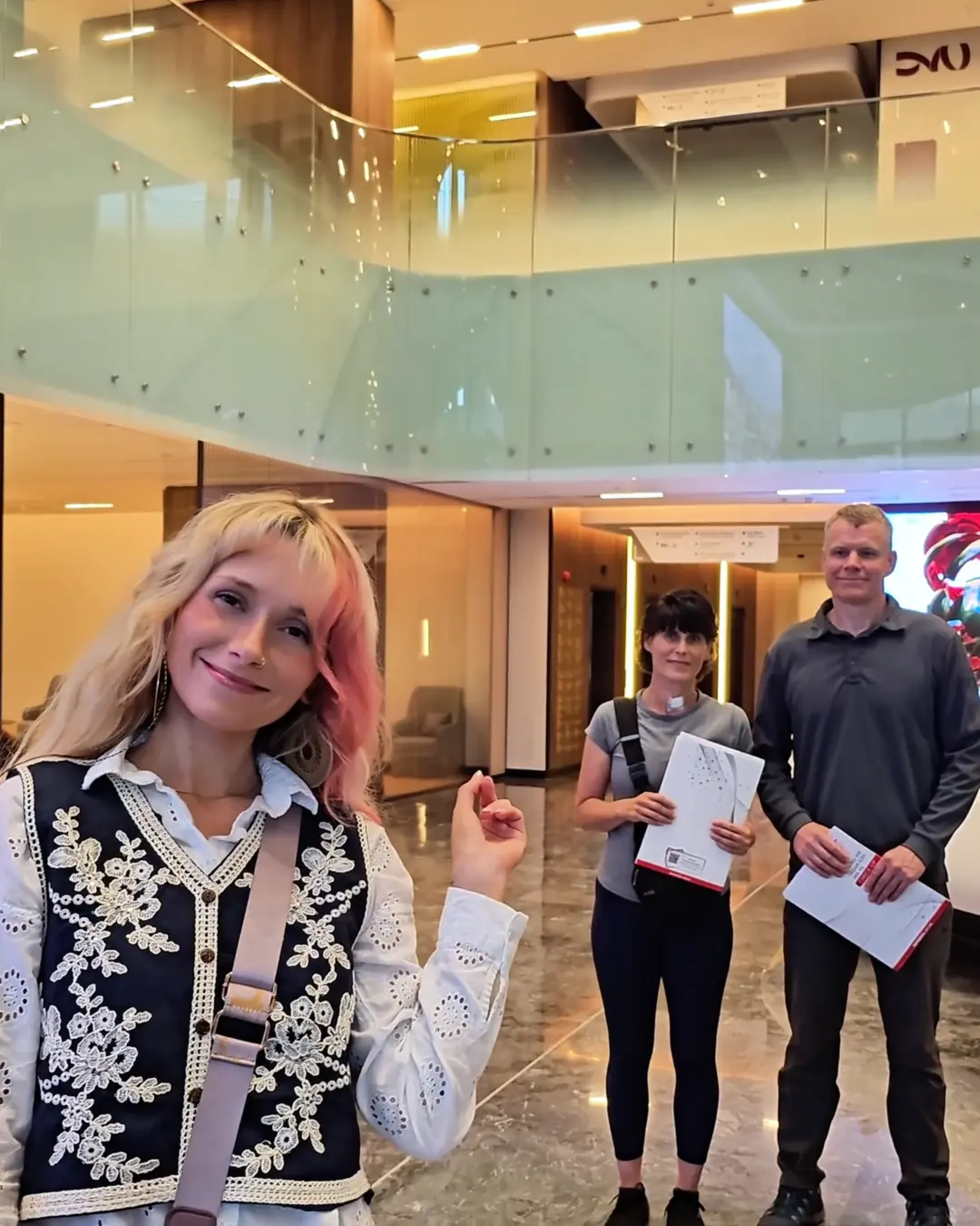 Woman posing in a modern hospital lobby in Istanbul with two adults holding paperwork in the background