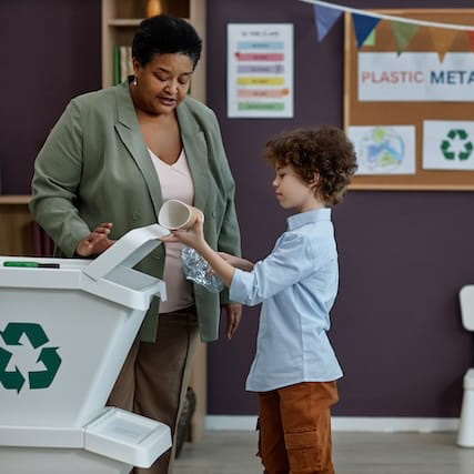 A black woman teaching a kid how to recycle in a school setting