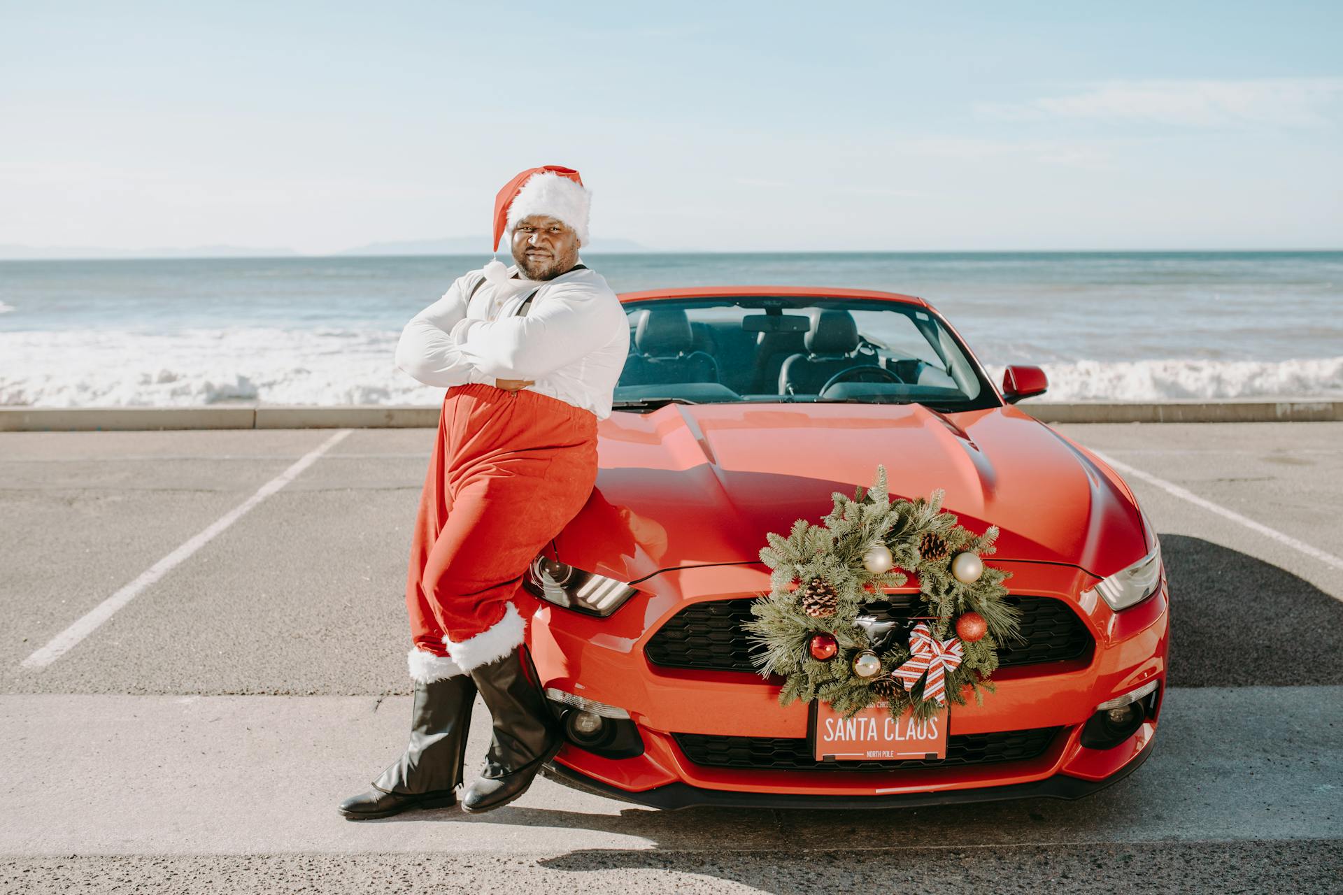 an African American santa sitting on a red sports car