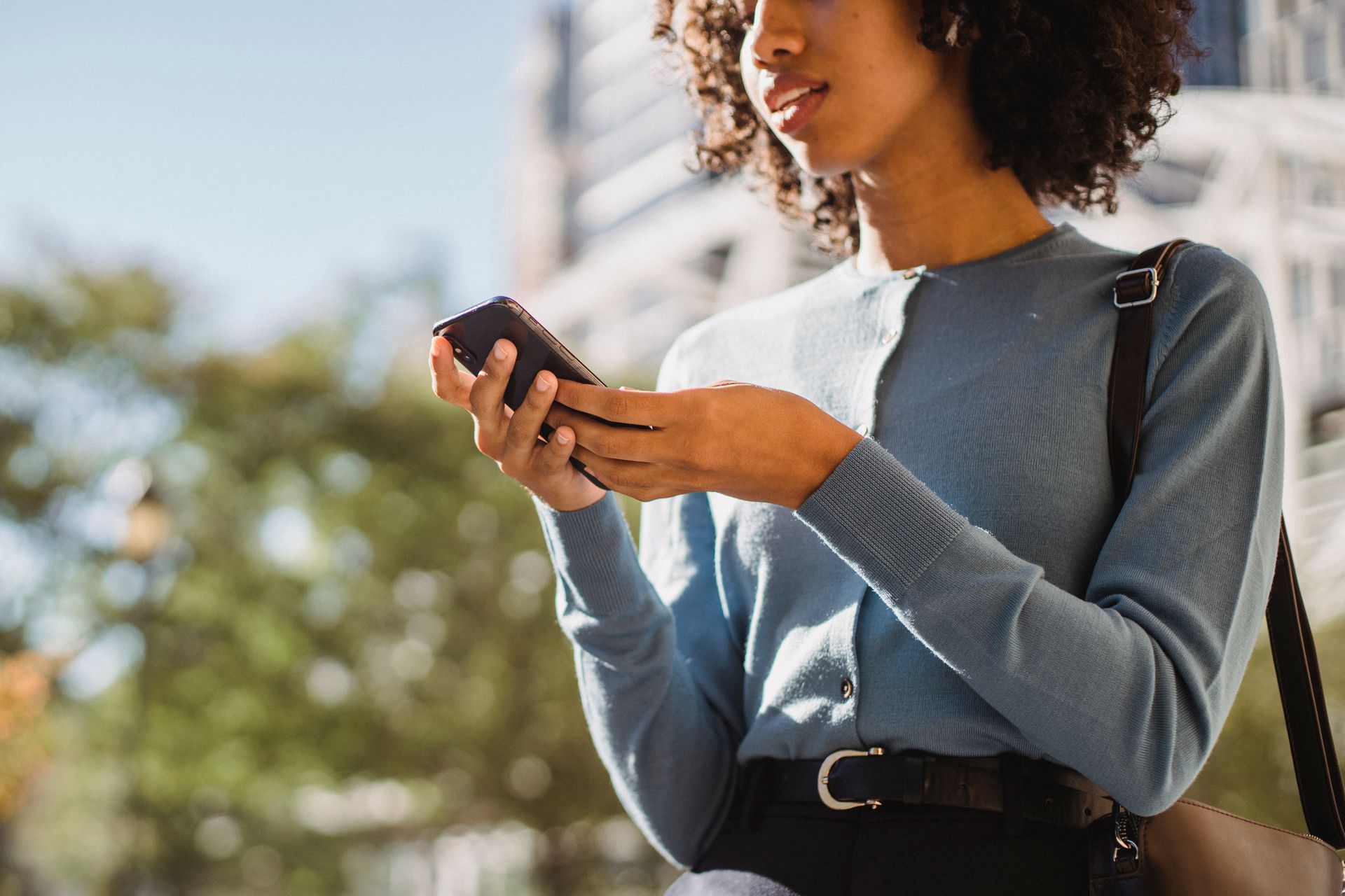 woman in blue sweater looking at smartphone