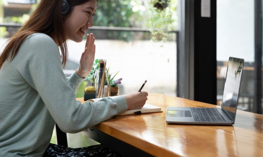 A person using a laptop and taking notes at a table, learning AI courses on Udemy and Coursera to future-proof her career.