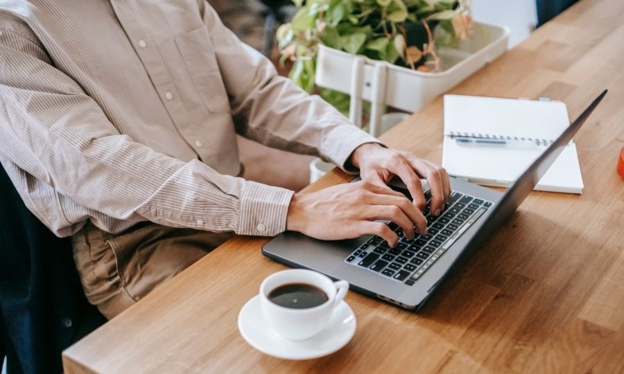 A man typing on a laptop with a coffee cup, using AI-powered tools for enhanced productivity in future-proof USA freelance careers.