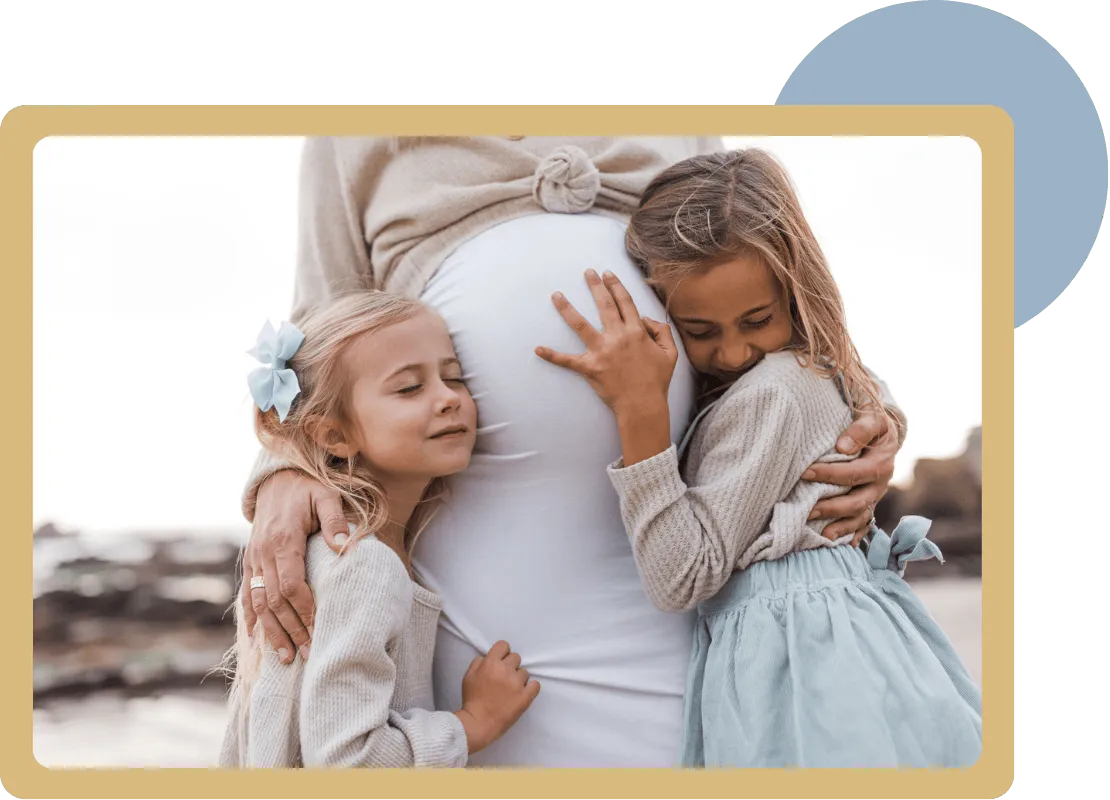 Two young girls hugging and resting their heads on a pregnant woman's belly, showing affection.