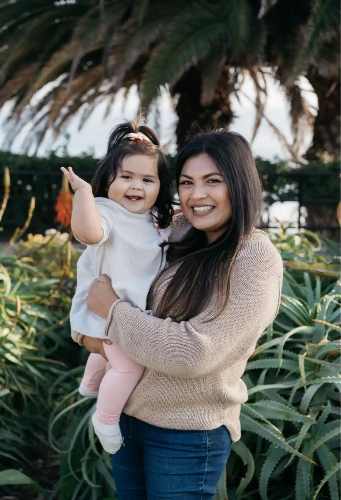 Smiling nanny or mother holding a happy toddler waving outdoors