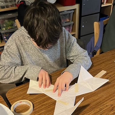 A long boy is focused, looking down at a the paper he is folding.