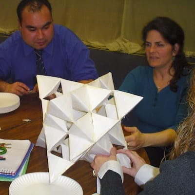 Three adults working on a paper folding sculpture about 1 foot in diameter during a wholemovement workshop.