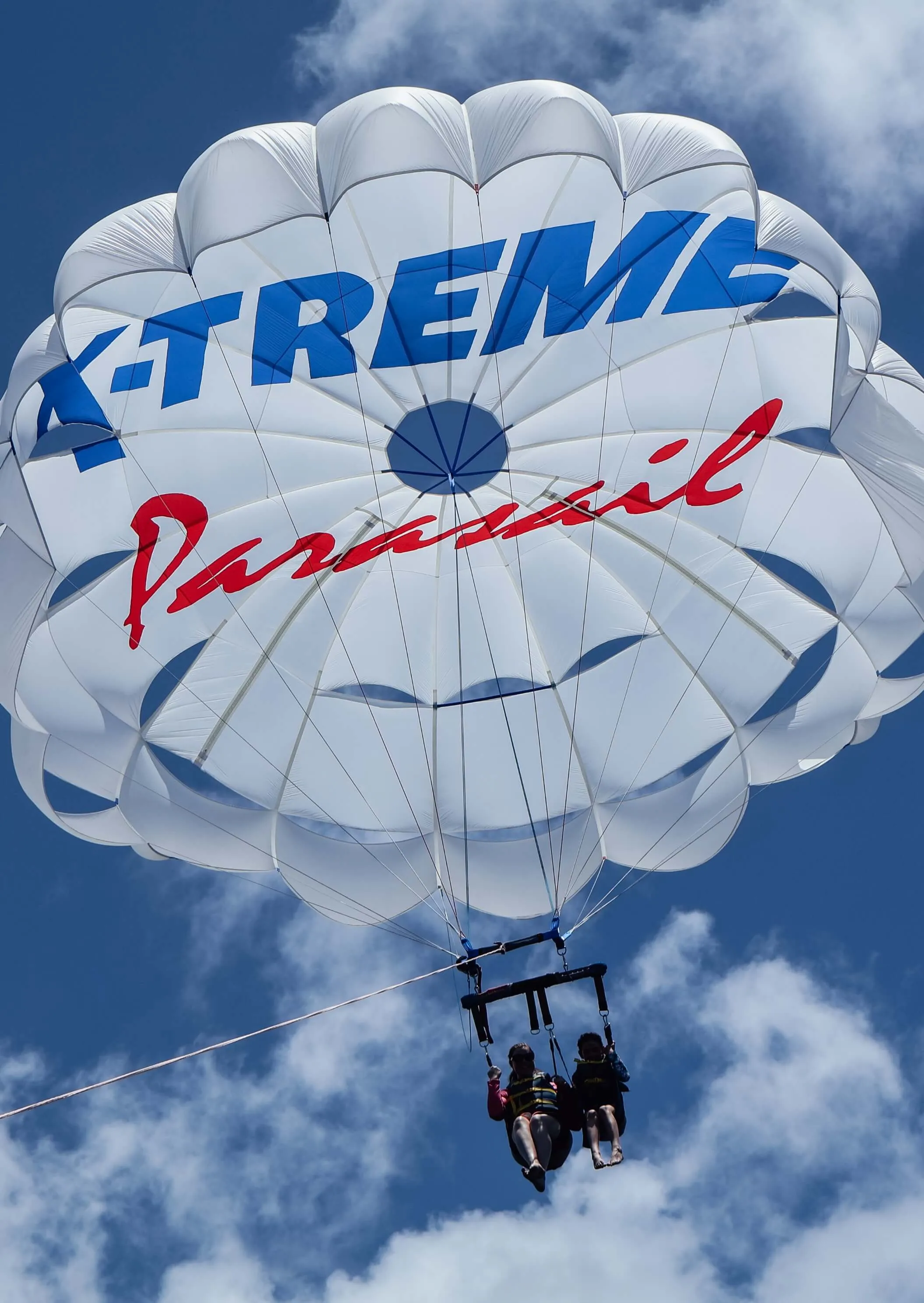 Two riders on a tandem flight high above Oʻahu beneath the branded X-Treme Parasail canopy