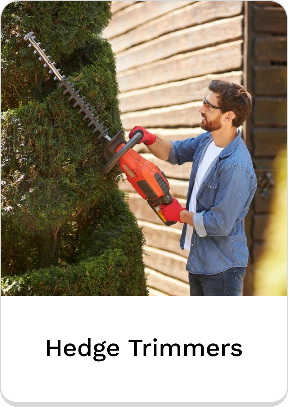 Man trimming hedges with electric hedge trimmers in a backyard garden.