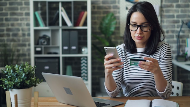 A merchant holding a credit card near a laptop while paying for web development services