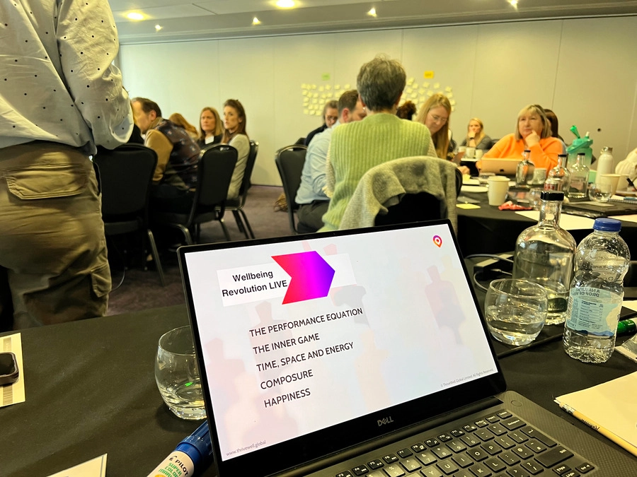 A laptop screen displays the agenda for “Wellbeing Revolution LIVE