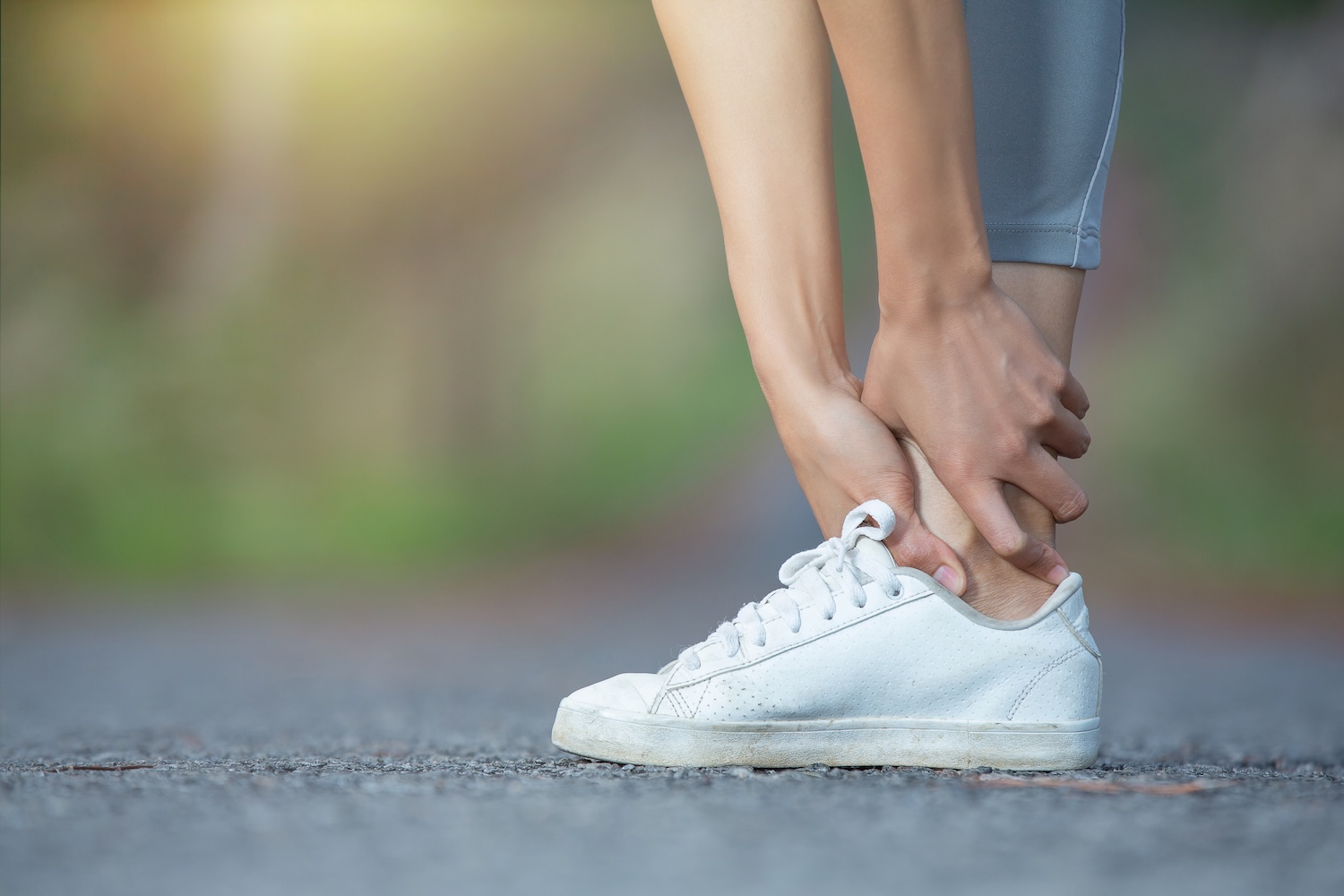 Eine Frau beim Joggen fasst sich mit beiden Händen an ihr Sprunggelenk.