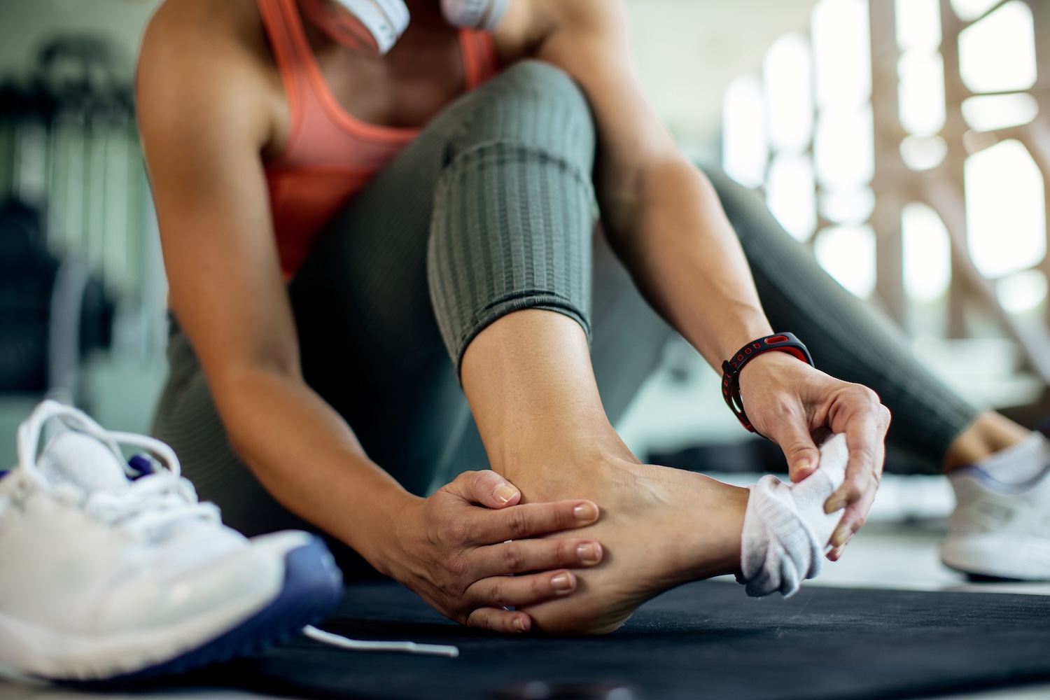 A woman in the gym sits on the floor and holds her ankle.