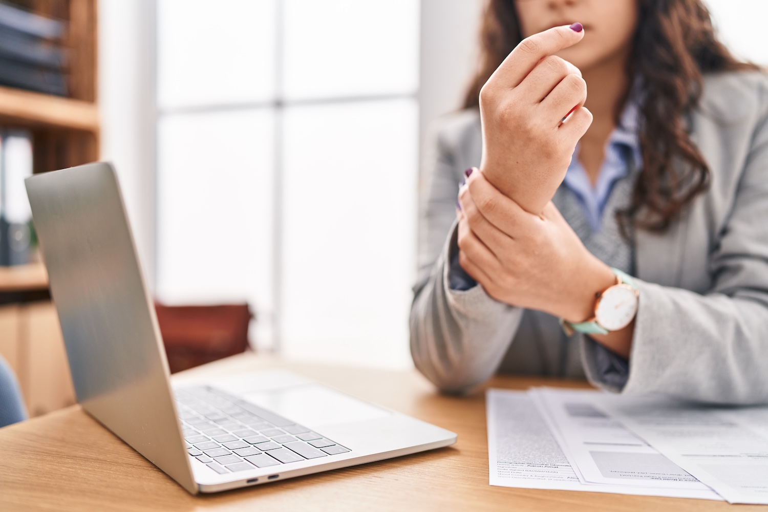 A woman sitting at her desk in the office, holding her wrist because she has wrist pain.