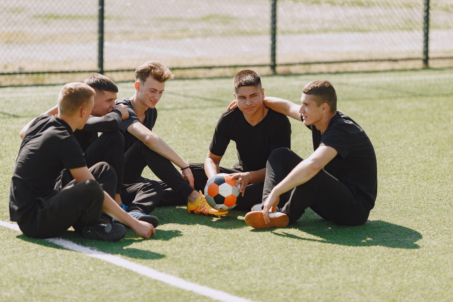 Fussballmannschaft sitzt nach dem Vereinstraining auf dem Spielfeld zusammen – physiotherapeutisch begleitetes Teamtraining bei PhysioWelt in Schlieren