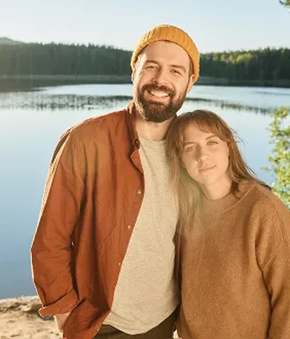 Couple standing together by a calm lake on a sunny day