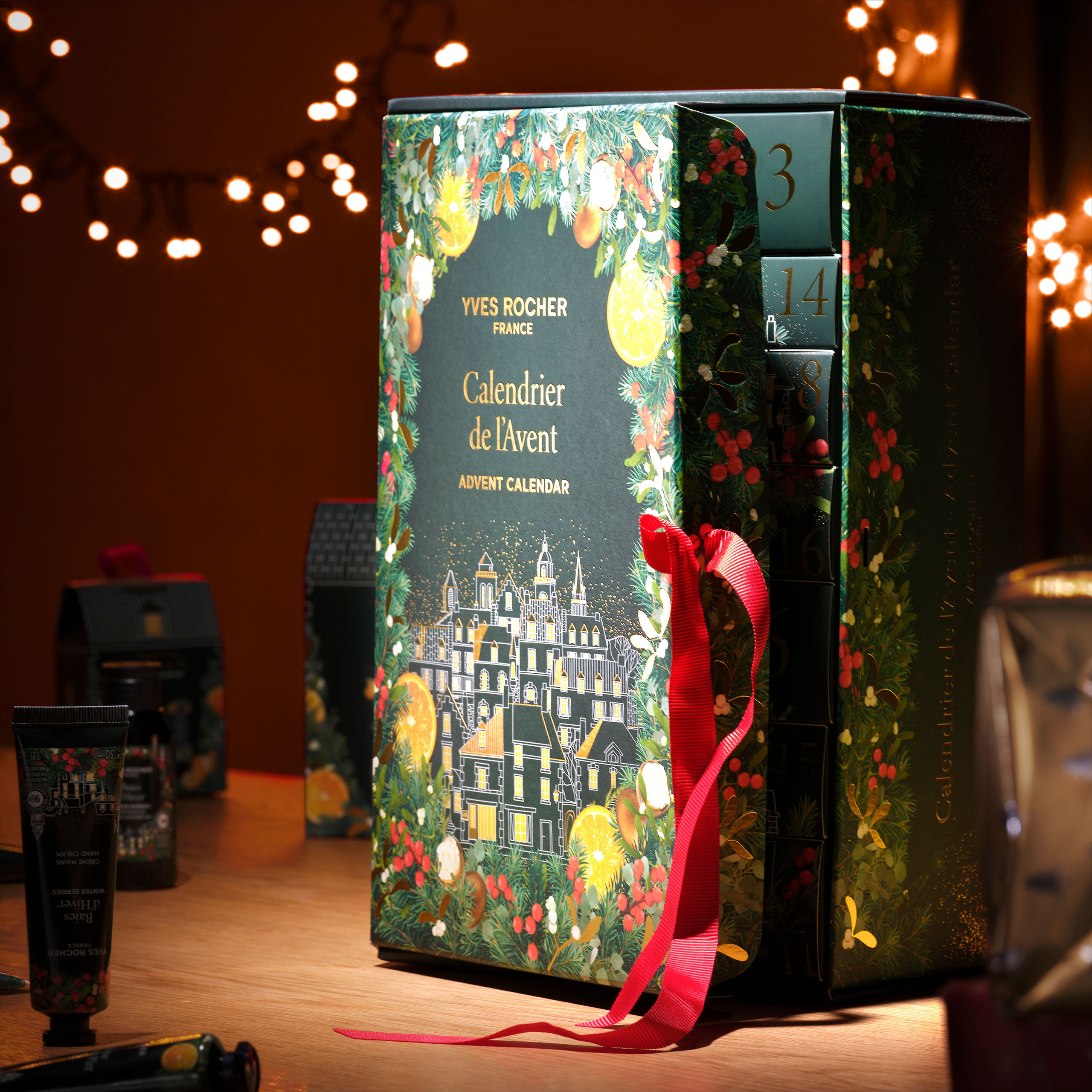 Yves Rocher 2025 Advent Calendar standing upright on a wooden surface, featuring an illustrated festive village design with botanical details and a red ribbon.
