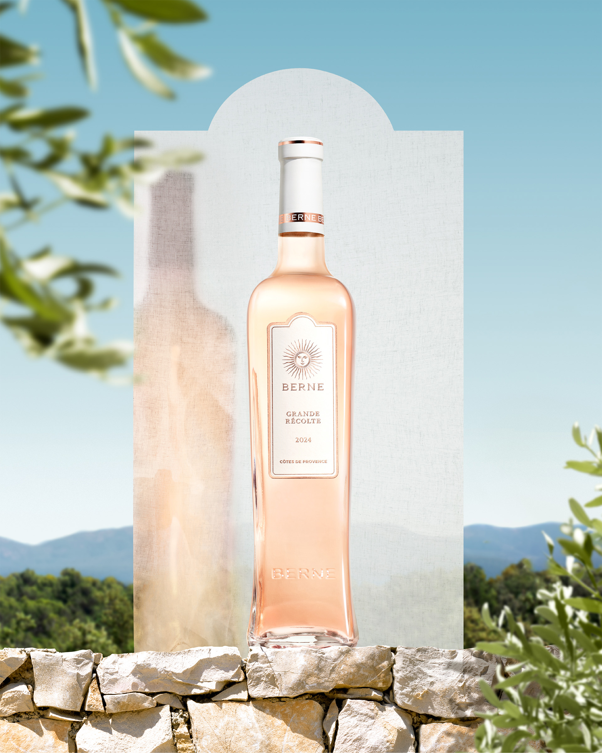 Rosé wine bottle from Château de Berne on a sunlit stone wall with Provence landscape backdrop