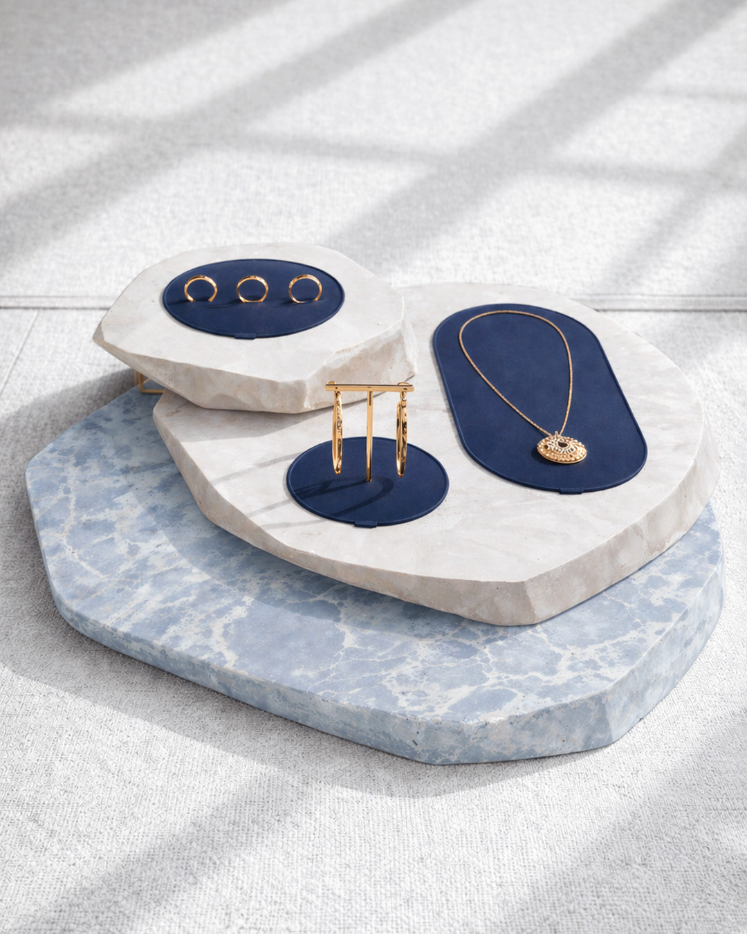 De Beers gold jewelry displayed on blue velvet pads over sculptural marble plinths.