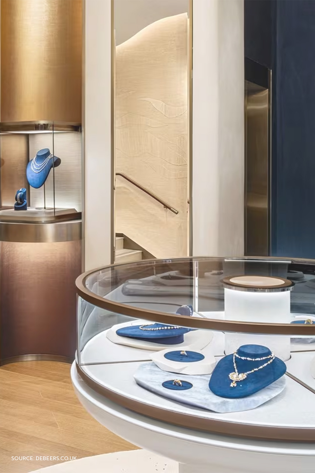 De Beers boutique interior with illuminated glass showcases and blue velvet fine jewelry displays.
