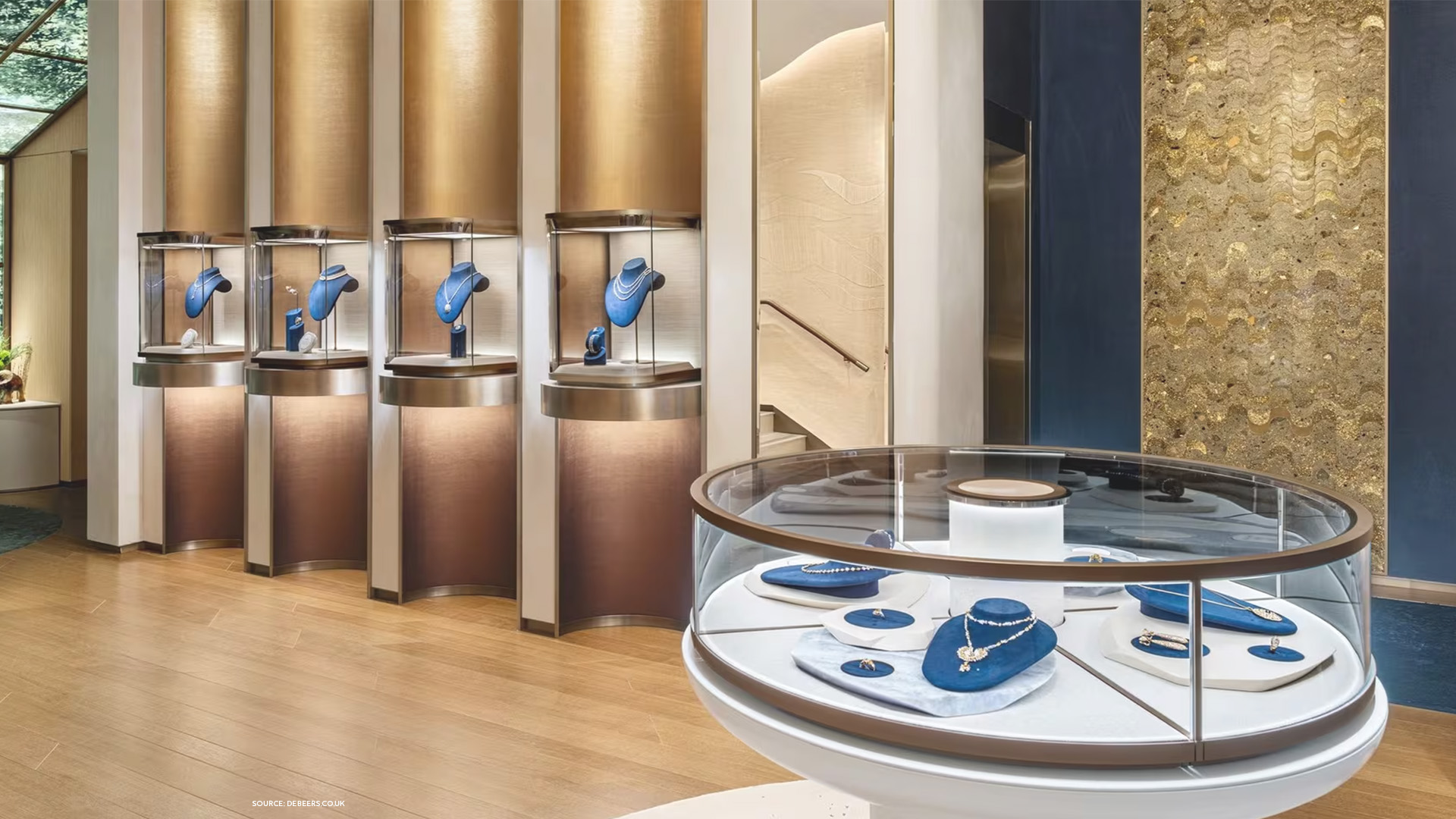 De Beers boutique interior with illuminated glass showcases and blue velvet fine jewelry displays.