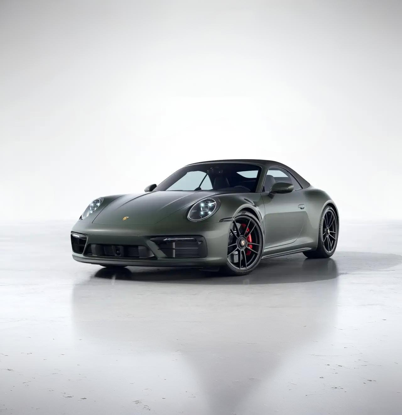 Dark green Porsche 911 sports car parked on a reflective white studio floor.