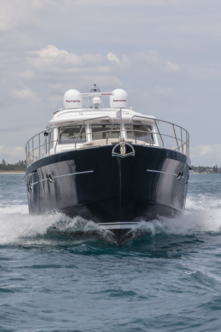 Front view of a black and white motor yacht creating waves as it moves through the water.