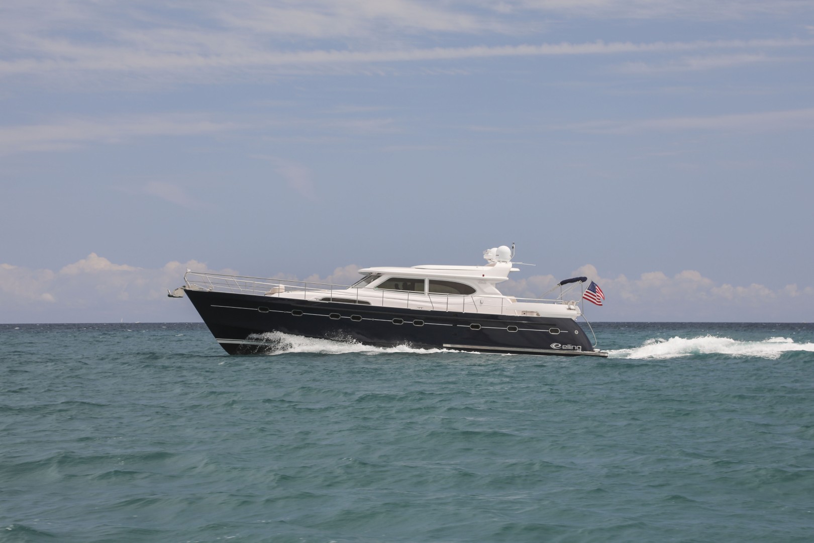 Black and white motor yacht cruising on calm ocean waters under a partly cloudy sky.