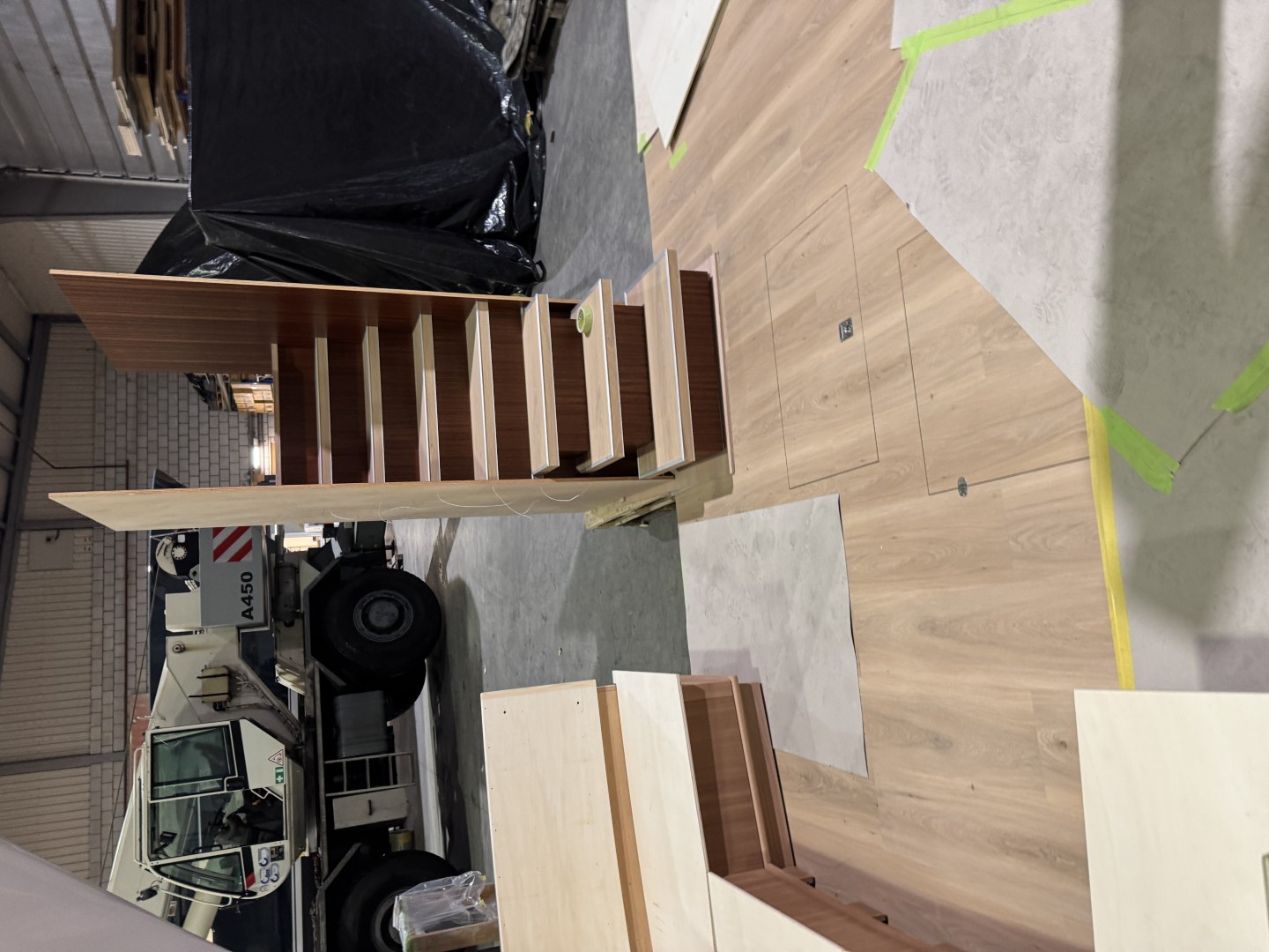 Wooden staircase structure with light wood steps and dark wood sides, set on light wood flooring in an industrial warehouse.