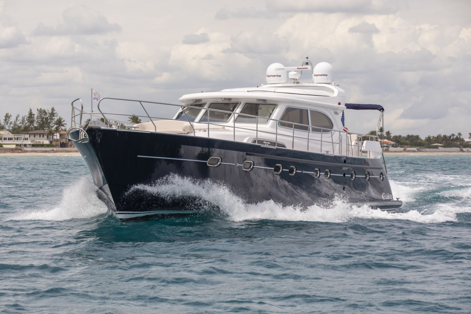 Dark blue and white luxury motor yacht cruising on water with waves breaking along its hull.