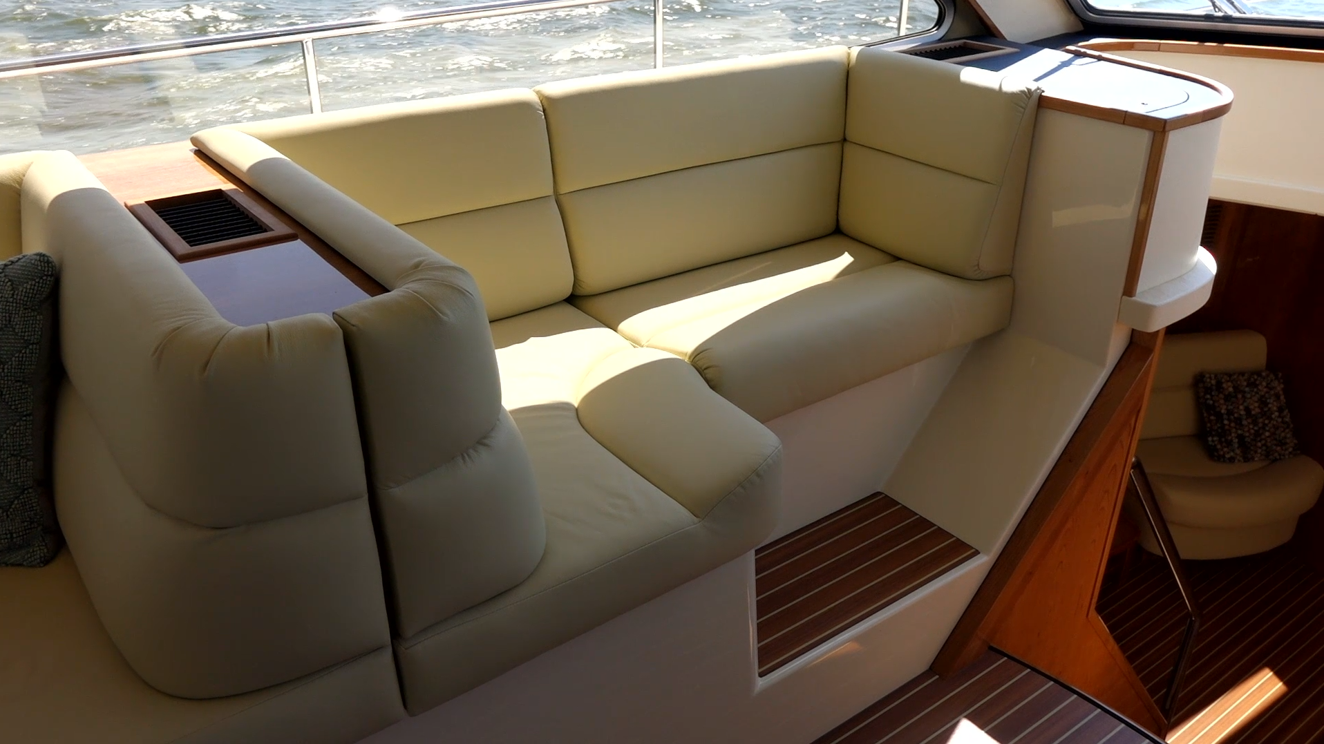 Beige leather cushioned seating area on a boat with wooden accents and water visible outside the railing.