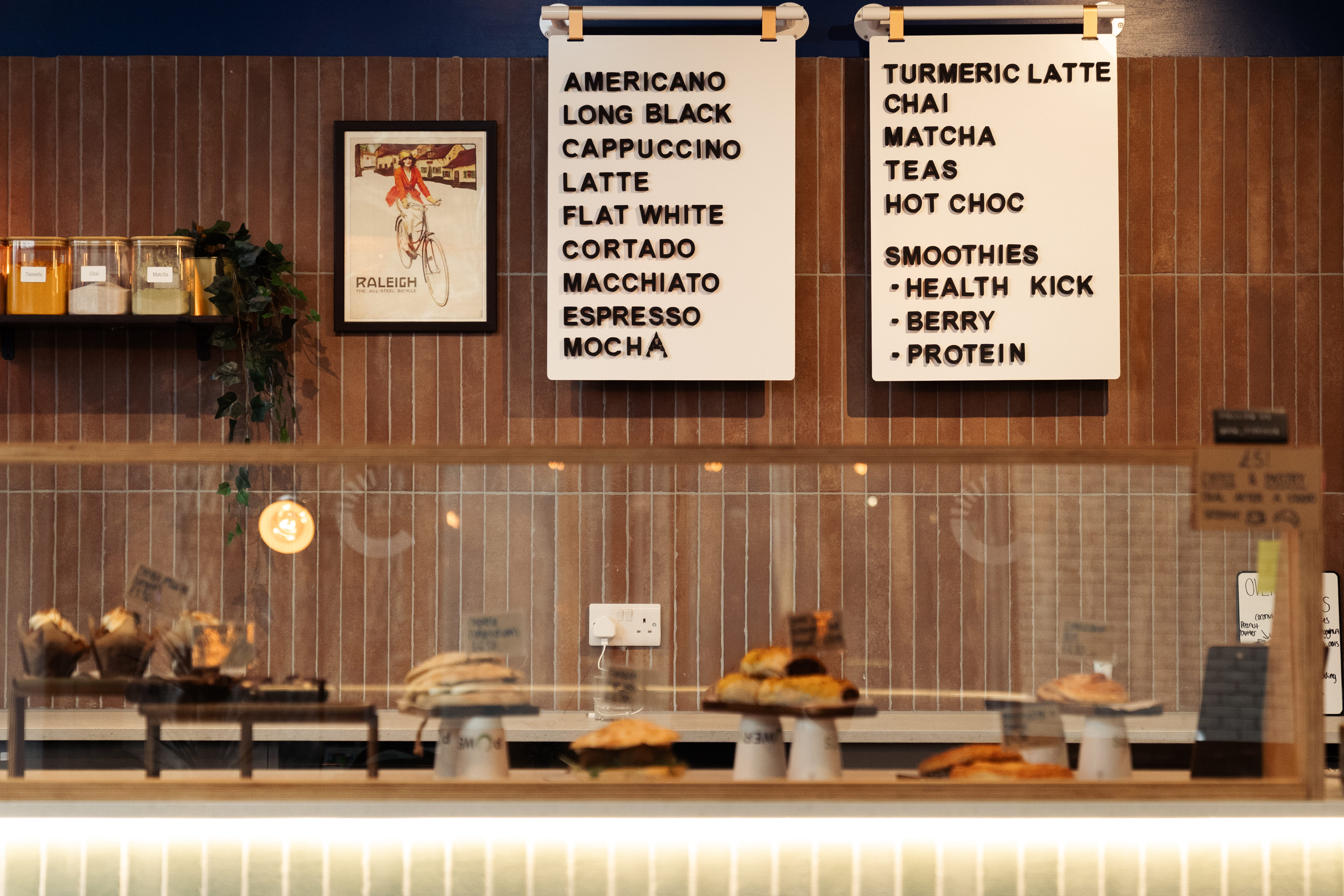 close up of cafe counter wall with lots of wooden texture, a drinks board on the wall, and a glass counter with cakes