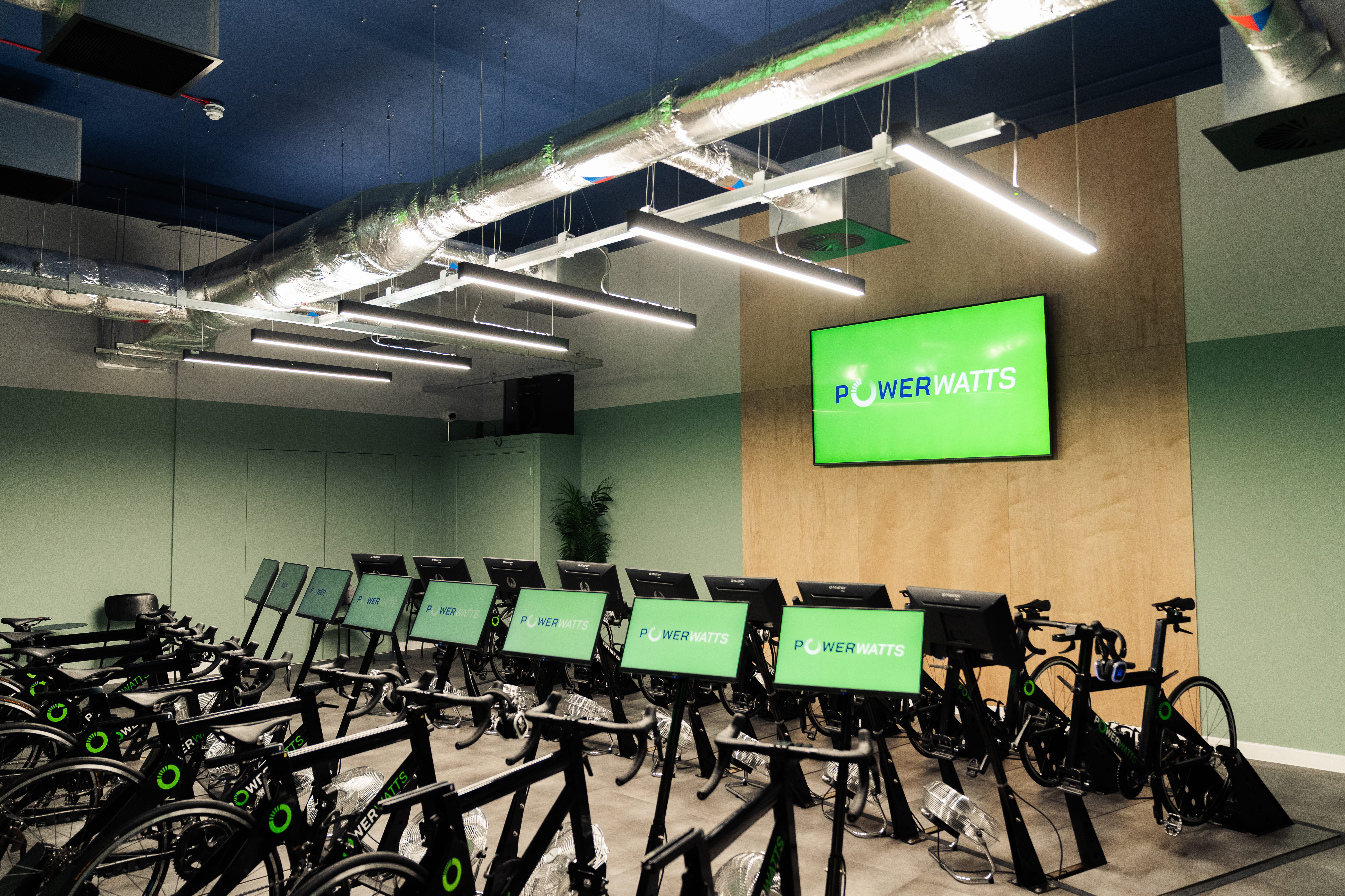 two rows of indoor cycles with green screens and PowerWatts logo