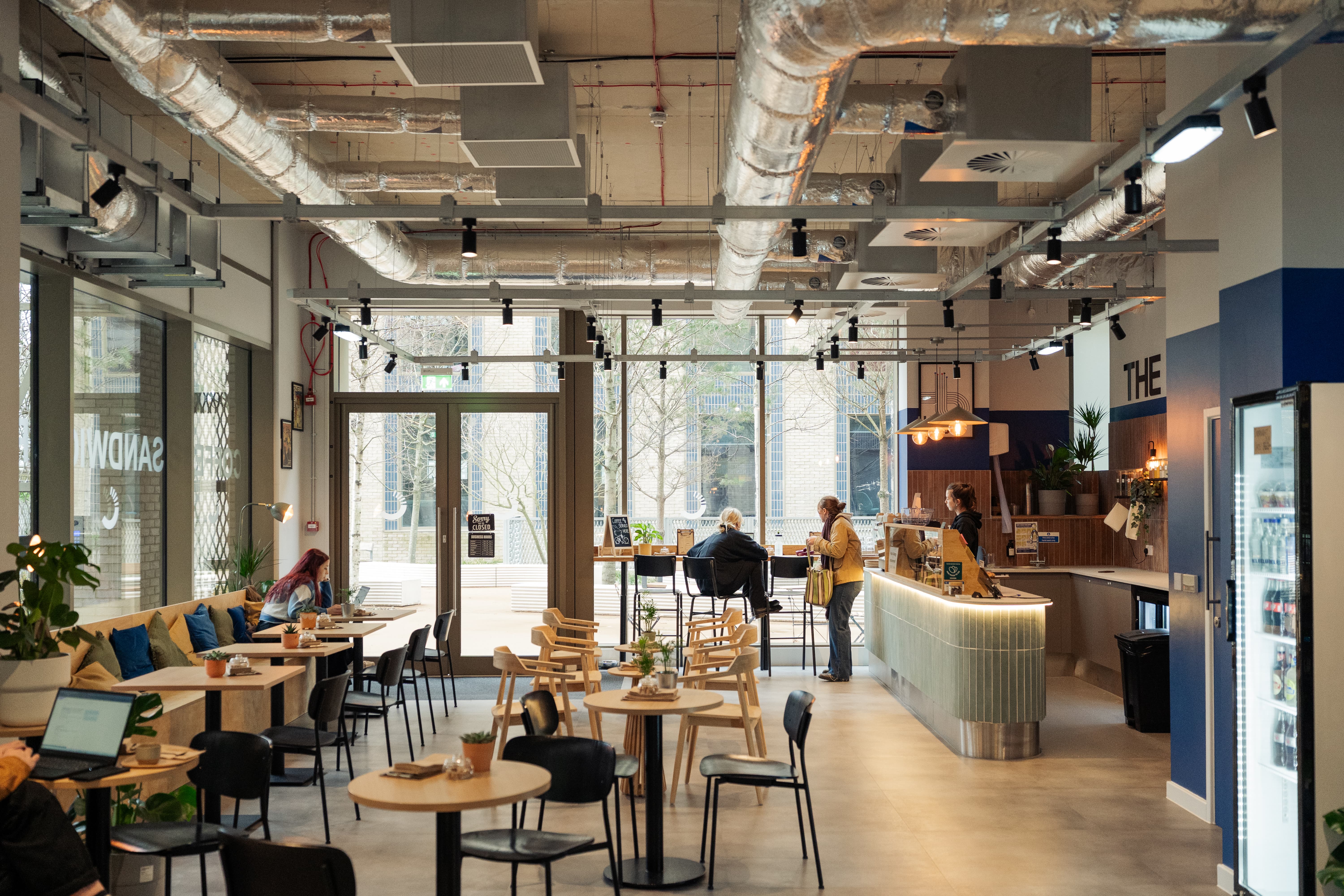 big cafe with big glass window in background, lots of wooden tables and chairs