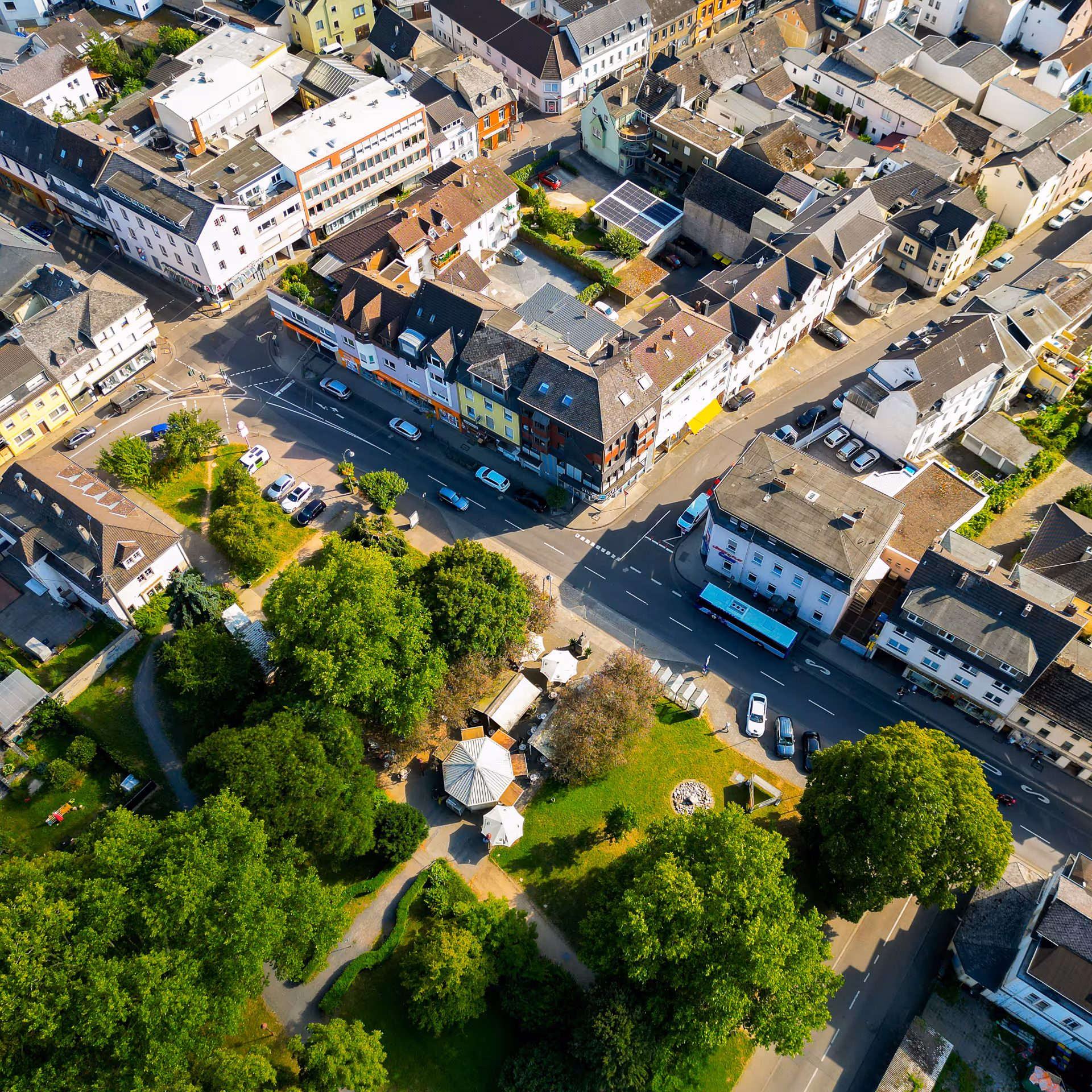 Luftaufnahme einer Stadt mit Wohnhäusern, einer Straße mit Autos und einem grünen Park mit Bäumen und Pavillons.