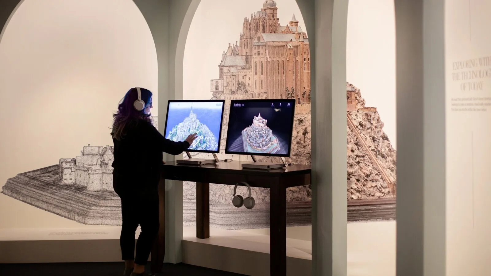 Visiteuse utilisant une tablette interactive présentant le portage de l’expérience HoloLens du Mont Saint-Michel, avec modélisation 3D de la maquette historique.