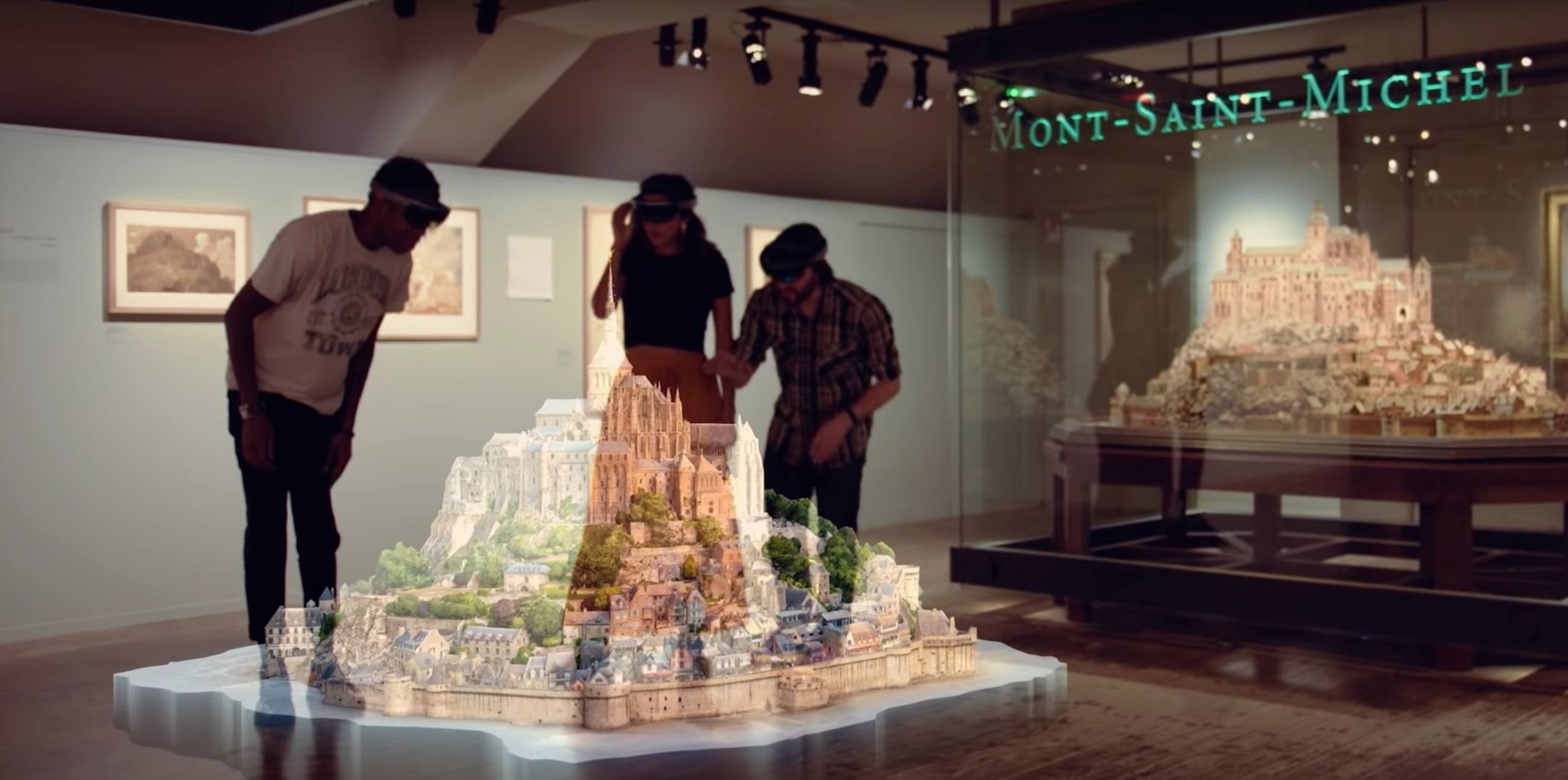 Three visitors equipped with Microsoft HoloLens headsets discover a mixed reality reconstruction of Mont Saint-Michel in a museum, with the historical model on display in the background