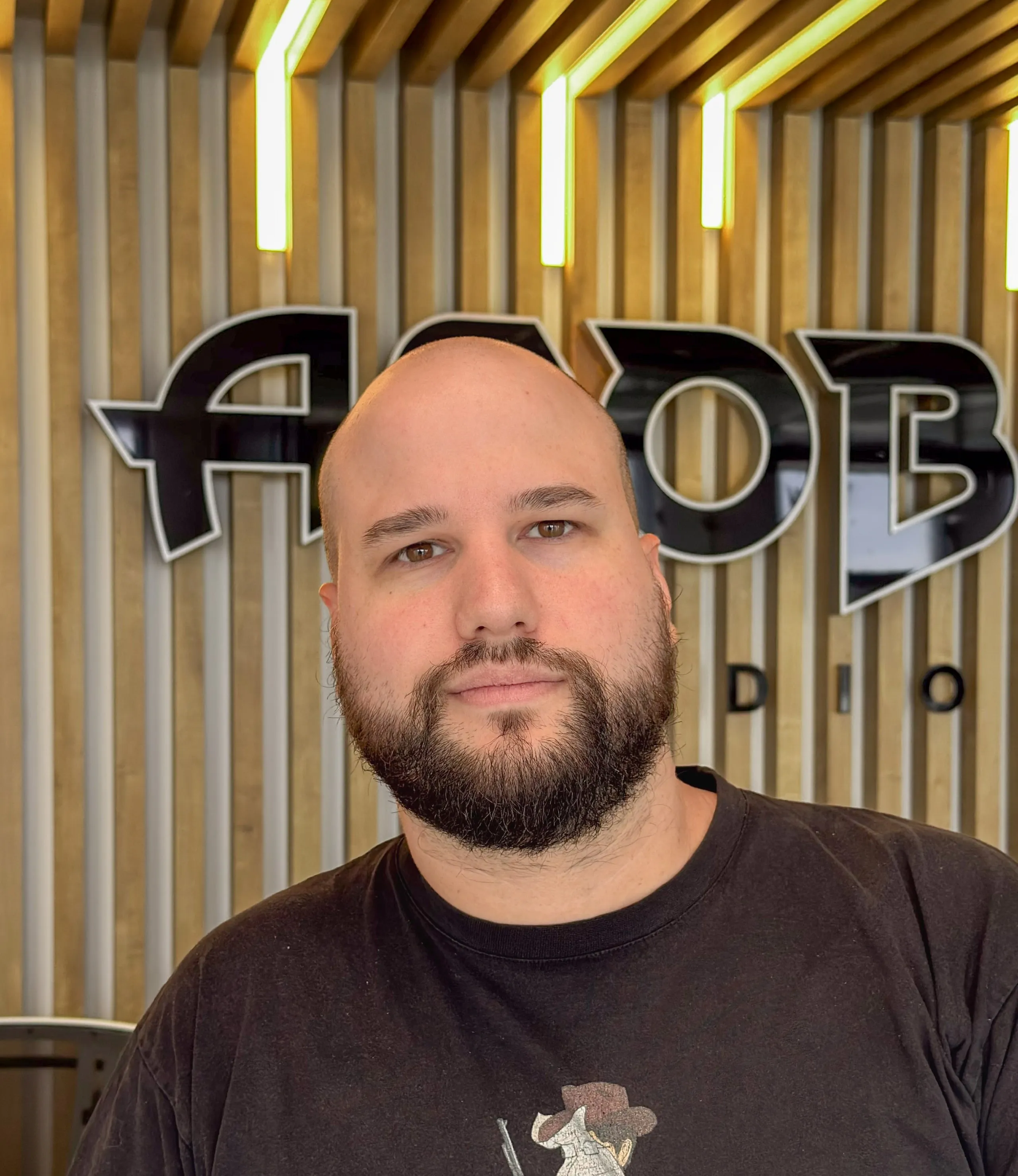 Portrait de Remi Garde d’Asobo Studio devant le logo de l’entreprise, dans un environnement moderne avec éclairage vertical et fond en bois clair.