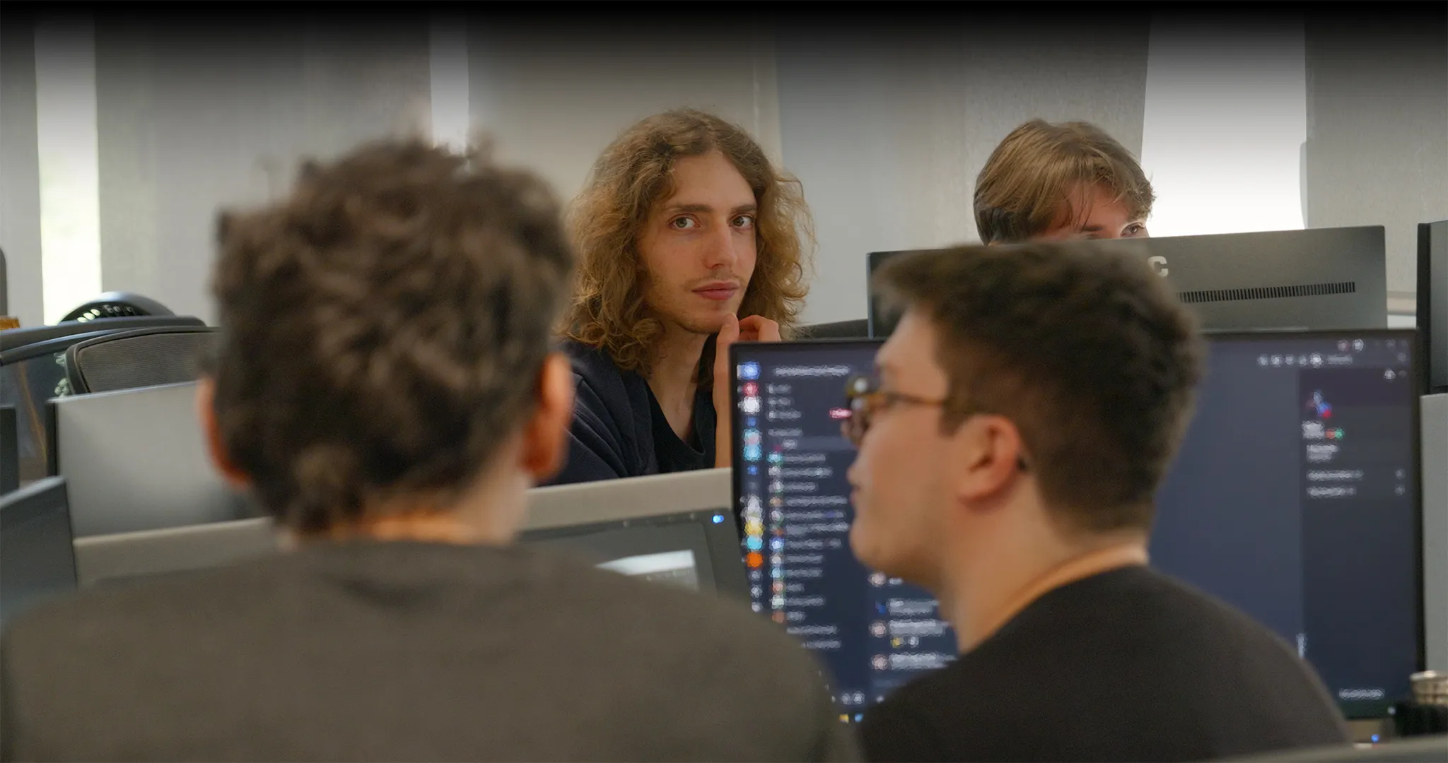 Groupe de développeurs en discussion devant leurs écrans dans l'open space moderne d'HoloForge