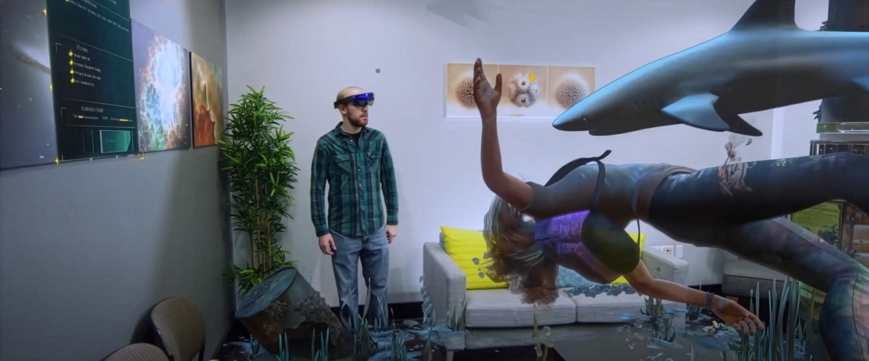 Homme portant un casque de réalité augmentée observant une scène holographique sous-marine avec plongeuse et requin dans un salon.