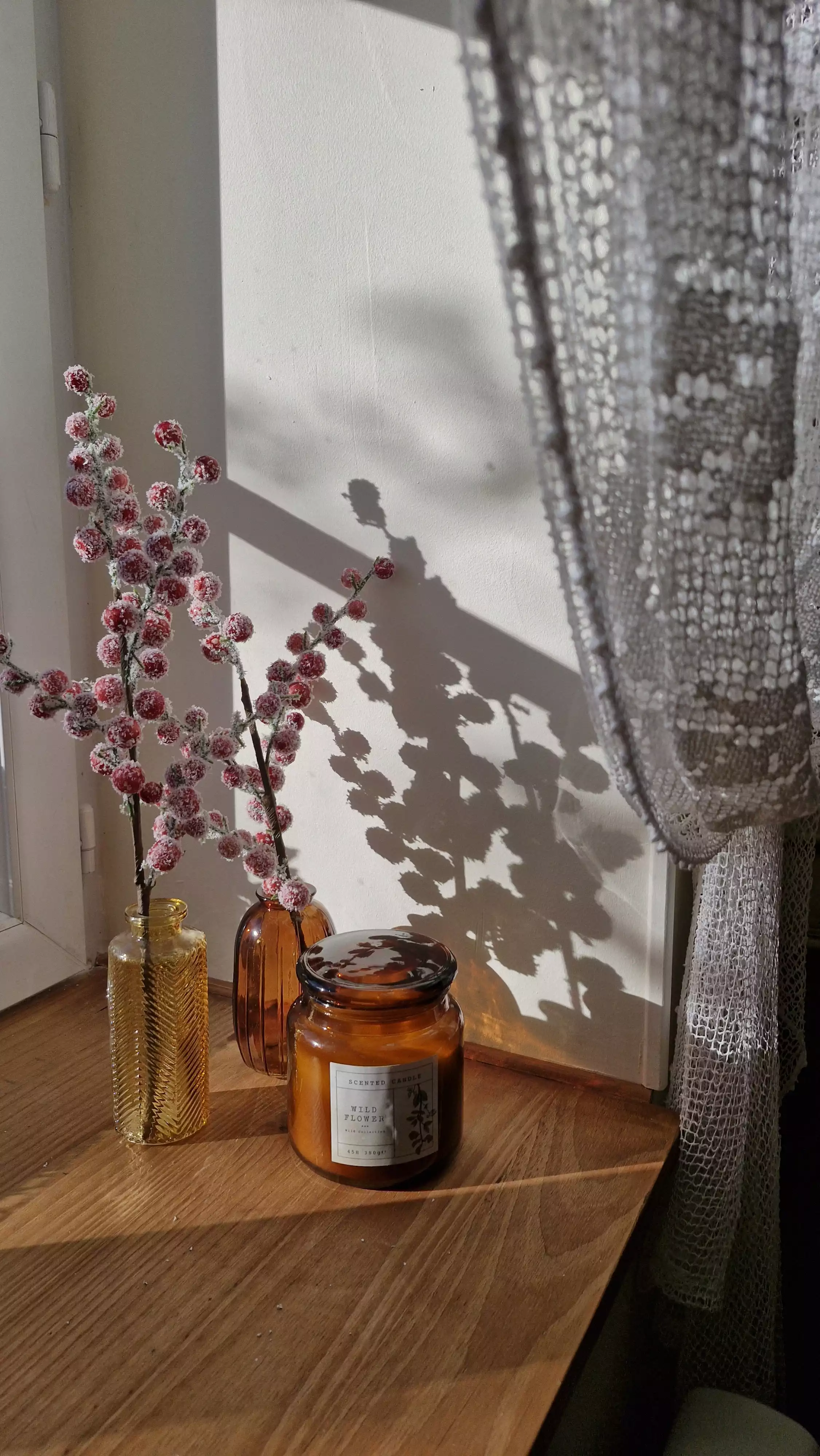 Photo d'une bougie et de brindilles posées sur le rebord de fenêtre, dont les ombres délicates sont projetées sur le mur