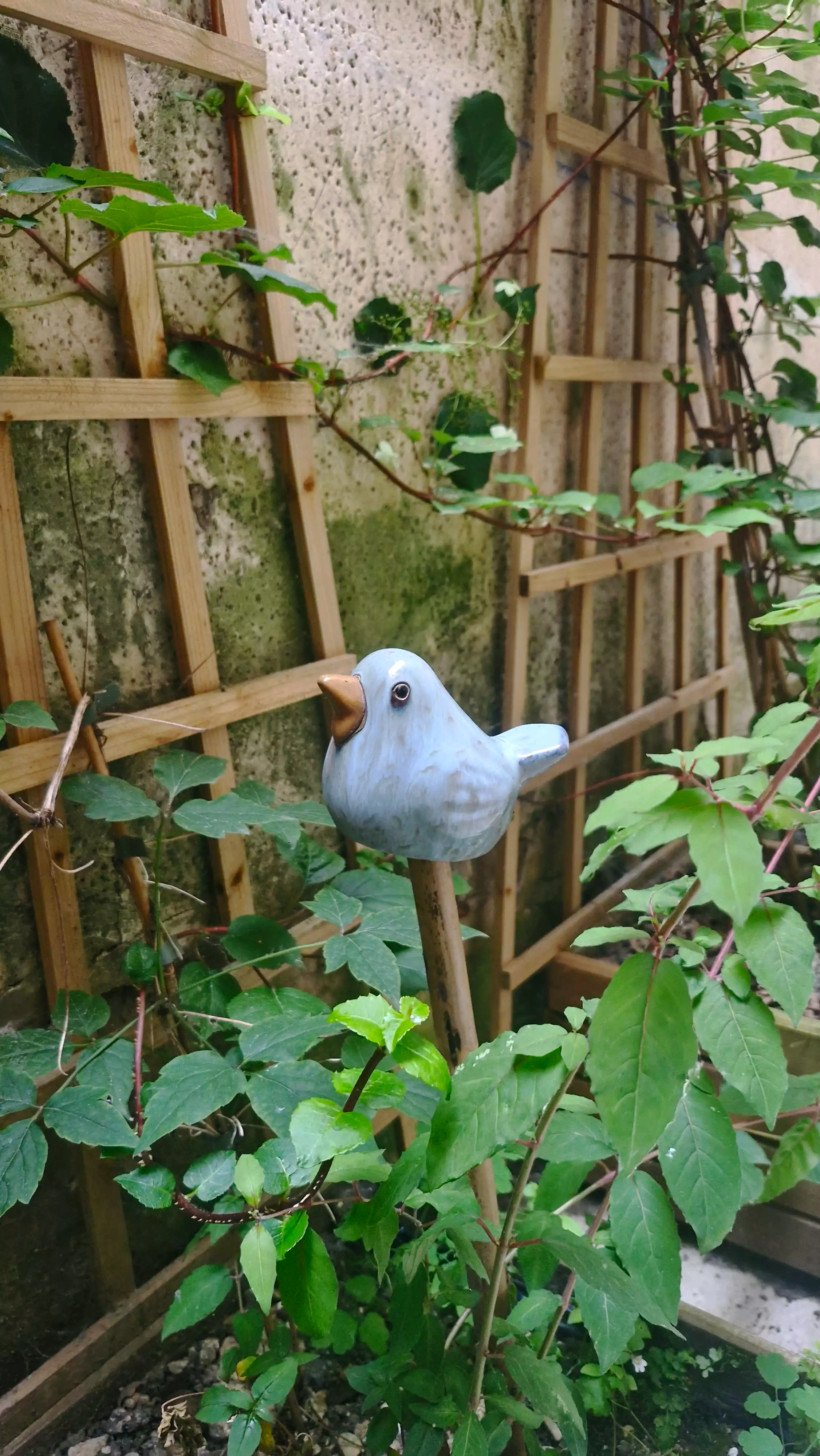 Photo d'un petit oiseau métallique bleu, planté dans les pots de fleurs du patio