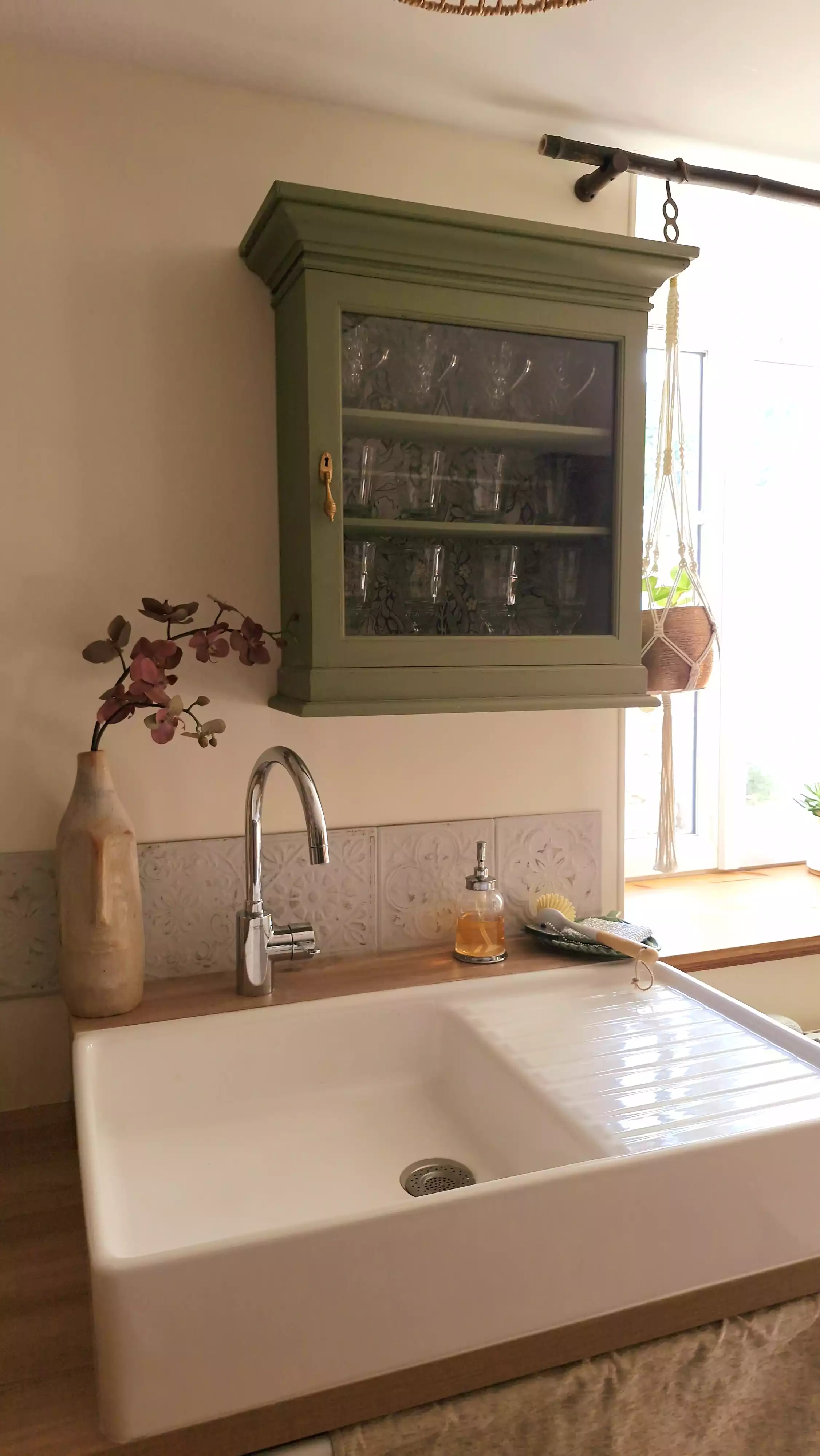 Photo d'un détail de la cuisine, l'évier en céramique sous un petit cabinet vert et une fenêtre donnant sur le jardin