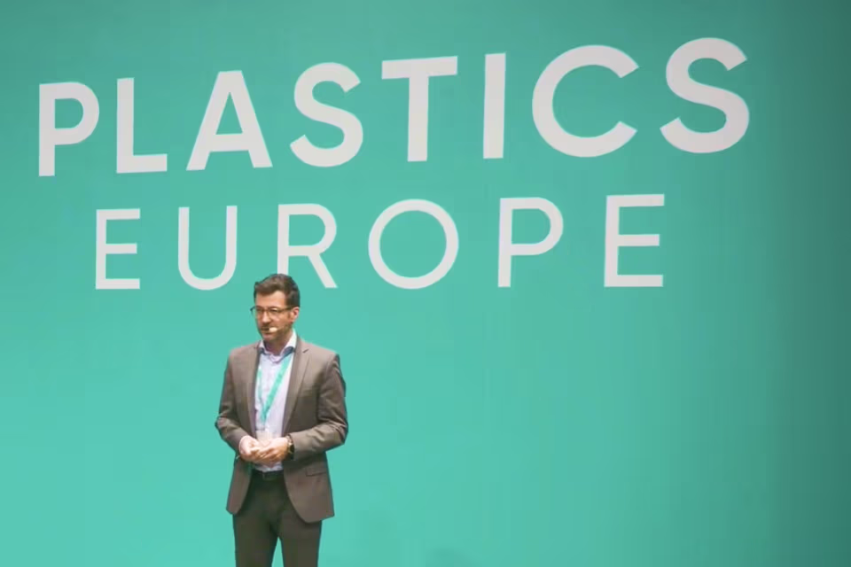 Ein Mann in Anzug spricht vor einer grünen Wand mit dem Schriftzug Plastics Europe.